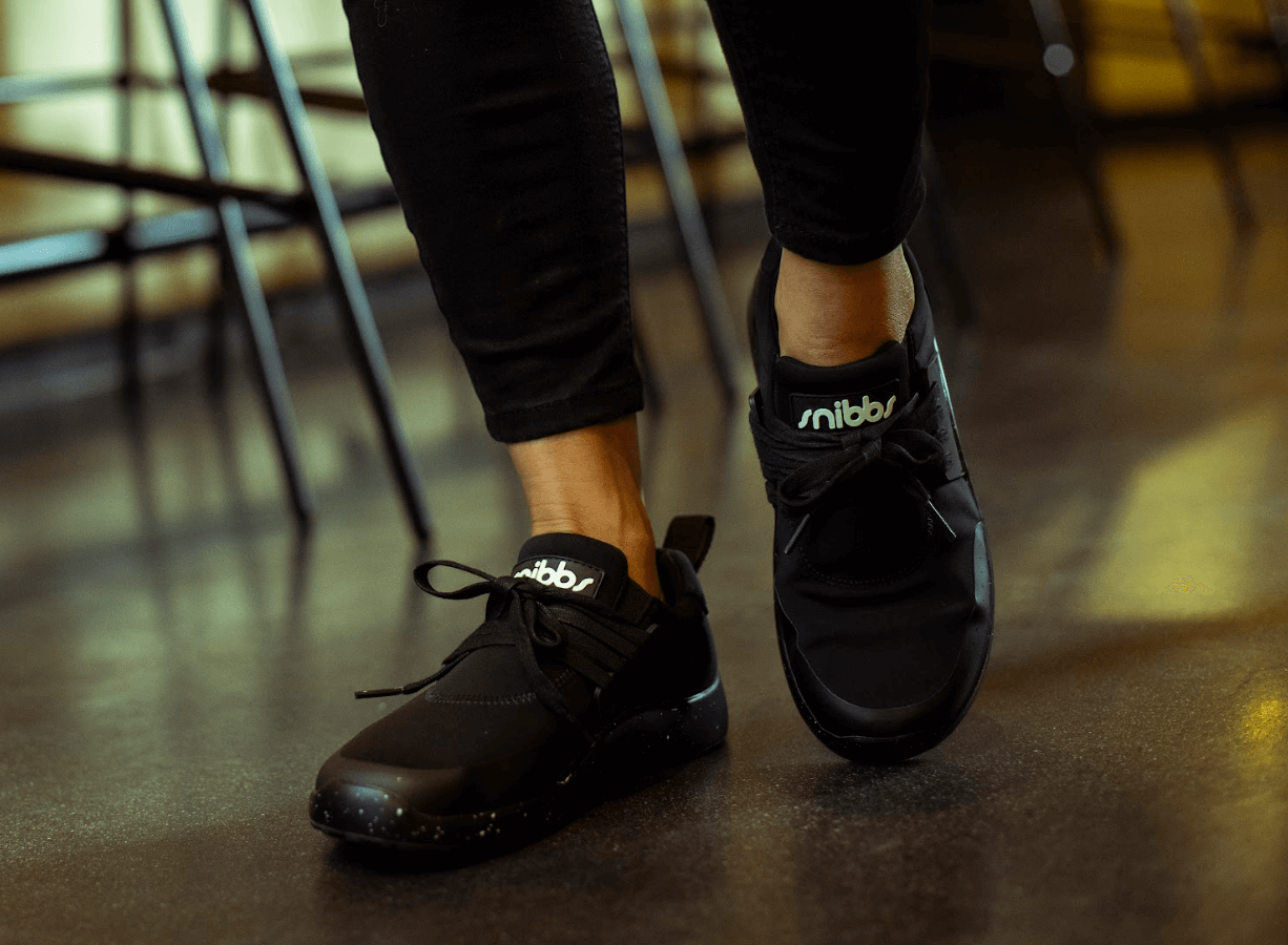 Person wearing black sneakers with 'snibbs' logo on shiny floor.