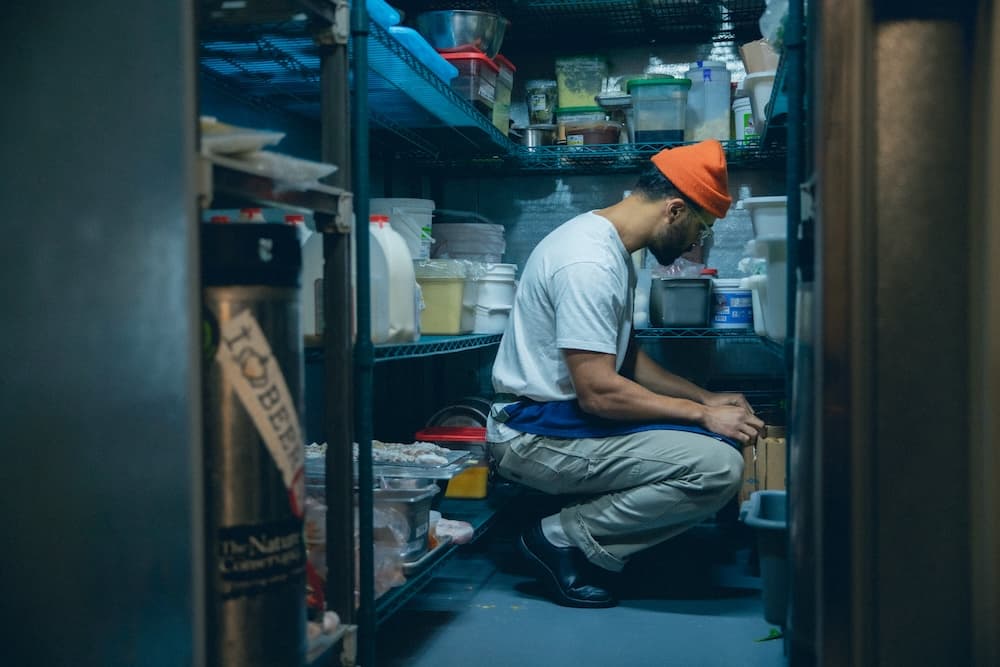 Man organizing items in a storage room, wearing a white shirt and orange beanie.