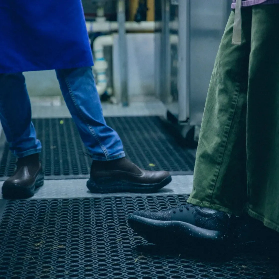 Two people standing in a kitchen wearing rubber-soled shoes and different colored pants.
